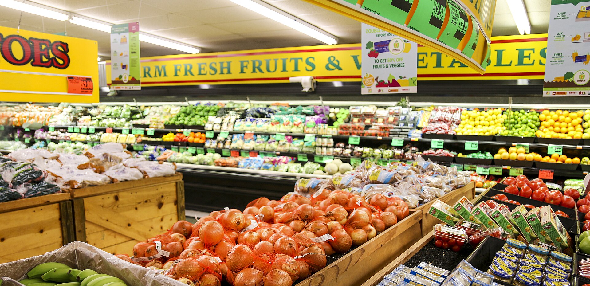 grocery-prices-factcheck Produce aisle of a discount grocery store, with bins of onions, bananas and tomatoes beneath a 'Farm Fresh Fruits & Vegetables' banner.